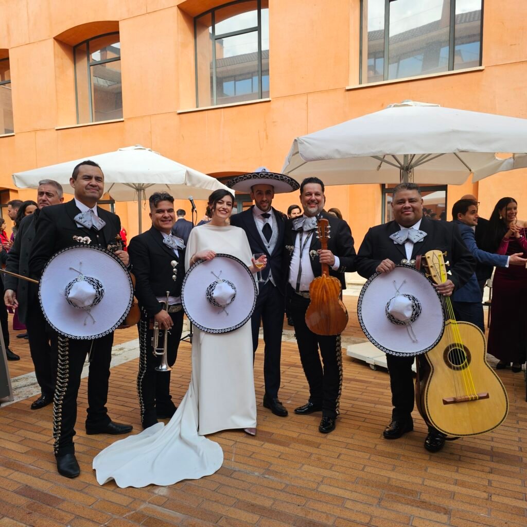 Grupo de mariachis con sombreros e instrumentos posa junto a una novia en un patio.