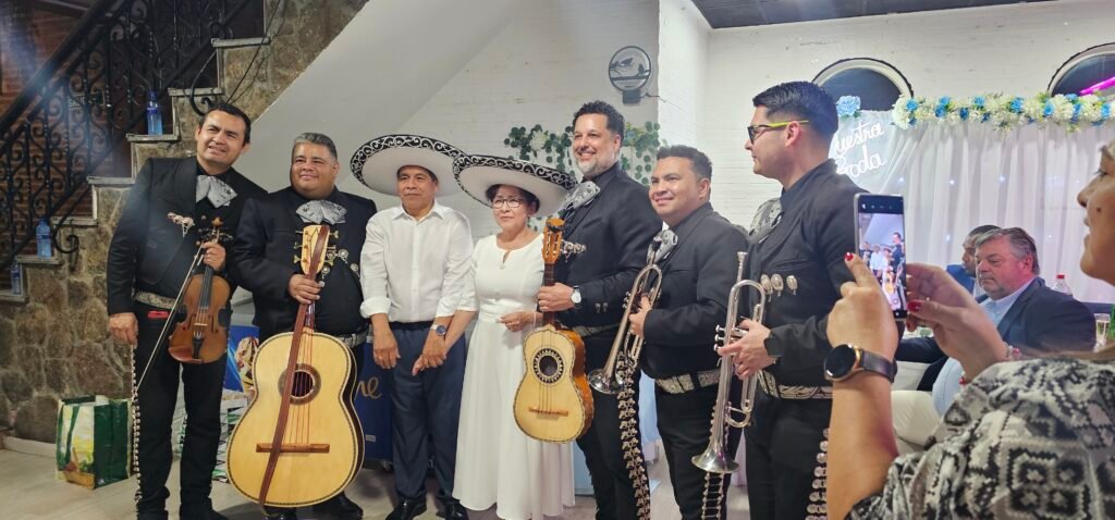 Músicos de mariachi con guitarra y trompetas junto a invitados con sombreros mexicanos.