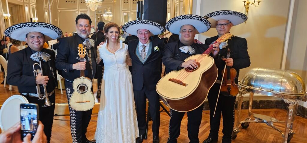Pareja de novios con un grupo de mariachis y sus instrumentos en un salón de celebración.