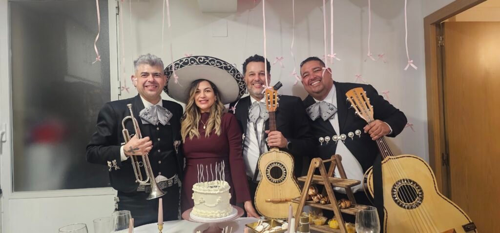 Tres mariachis posan junto a una mujer con sombrero y una tarta sobre la mesa.