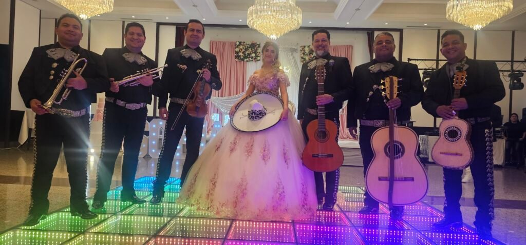Mariachis acompañan a una joven con vestido de fiesta y sombrero en un salón iluminado de colores.