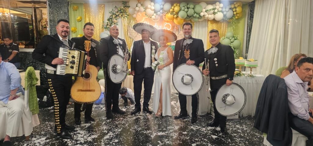 Mariachis con instrumentos y sombreros junto a los novios bajo una decoración floral.